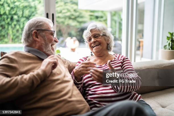 senior couple talking and celebrating good news at home - real people at home stock pictures, royalty-free photos & images