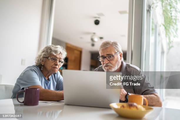 senior couple talking about home finances and using the laptop at home - demonstration against the marriage for all bill stock pictures, royalty-free photos & images
