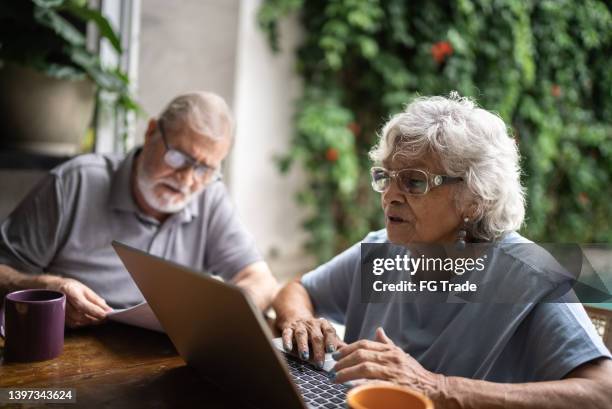 casal de idosos falando sobre finanças domésticas e usando o laptop em casa - idoso na internet - fotografias e filmes do acervo