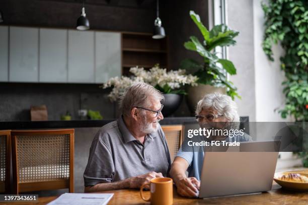 älteres paar, das über hausfinanzen spricht und den laptop zu hause benutzt - retirement planning stock-fotos und bilder