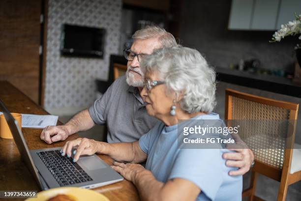 senior couple talking about home finances and using the laptop at home - baby boomer home stock pictures, royalty-free photos & images