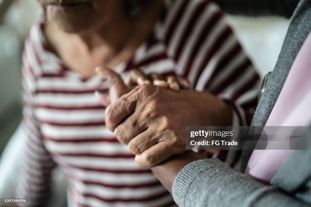Nurse or home caregiver and senior woman holding hands at home