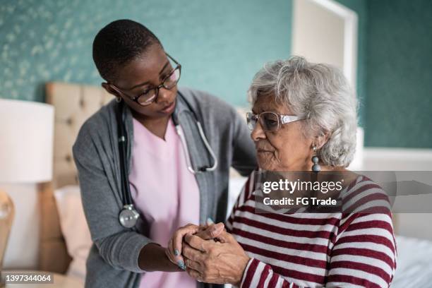 un soignant à domicile aide une femme âgée debout dans la chambre à coucher - aide patient médecin photos et images de collection