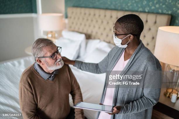 nurse using digital tablet and talking to patient at home - social worker mask stock pictures, royalty-free photos & images