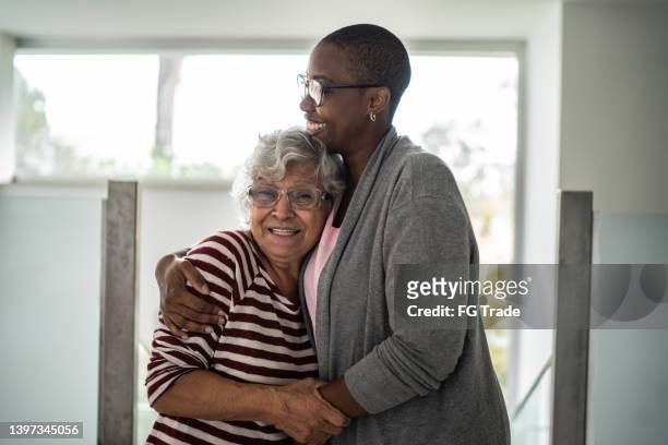 infermiera e donna anziana che abbracciano a casa - assistenza foto e immagini stock