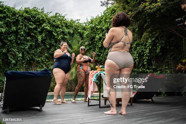 female friends dancing for social media and filming it on mobile phone in the pool at home - fat woman dancing stockfoto's en -beelden