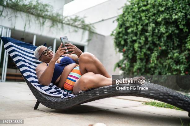 mature woman using the mobile phone in the pool at home - black women in bathing suit stock pictures, royalty-free photos & images