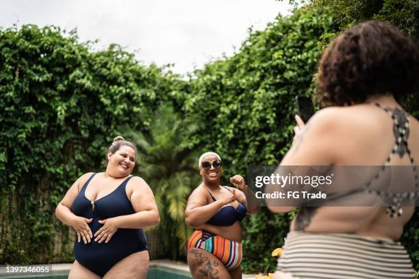 female friends dancing for social media and filming it on mobile phone in the pool at home - fat woman dancing stockfoto's en -beelden