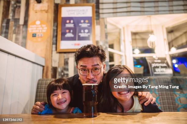 dad & daughters smiling joyfully at the camera while having meal in a restaurant - cosy pub stock pictures, royalty-free photos & images