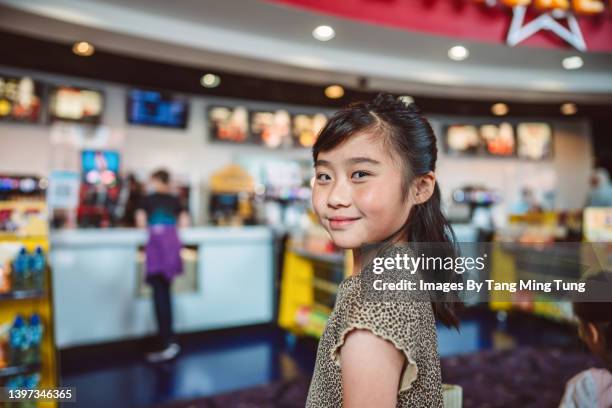 lovely girl smiling joyfully at the camera while queuing at the snack stand for popcorn before watching a movie in cinema - young & beautiful film stock pictures, royalty-free photos & images