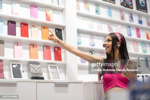 woman in a mobile phone and accessories store looks at the covers of the devices - exposant stockfoto's en -beelden