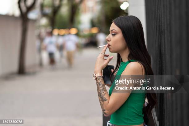 beautiful woman poses outdoors on the city street while smoking a cigarette - beautiful women smoking cigars 個照片及圖片檔