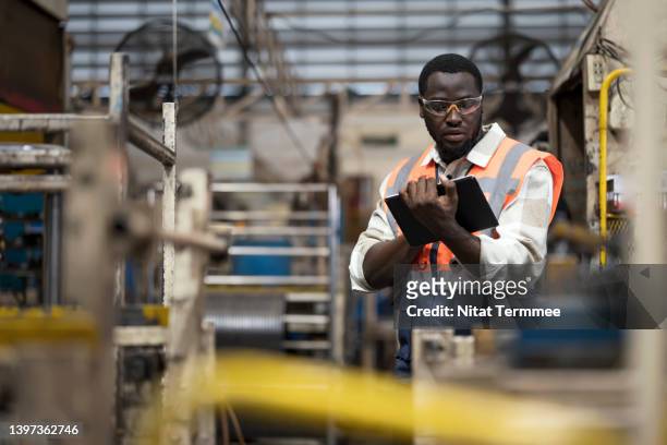 centralization maintenance management system in a manufacturing industry. male african maintenance engineer working in an engineering part production line while using mobile app on tablet to monitoring and working condition of a machinery. - auto cad stock pictures, royalty-free photos & images
