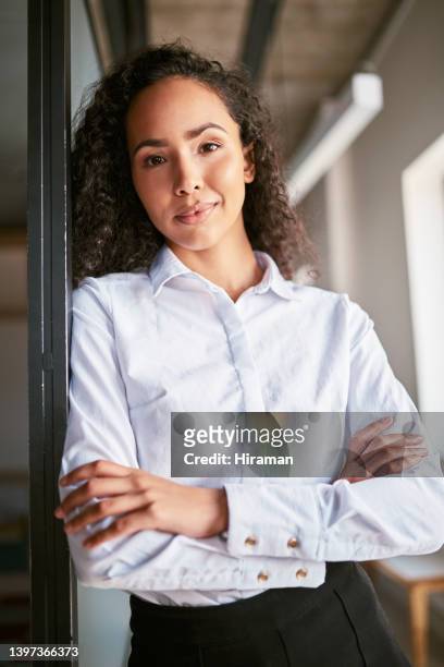 portrait of confident young mixed race female only business woman standing alone in her office with her arms folded. ambitious hispanic entrepreneur posing with her arms crossed in her workplace - women arms crossed stock pictures, royalty-free photos & images