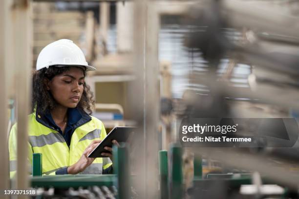 finished-product, first-pass quality in a manufacturing industry. female african american engineer working in an engineering part manufacturing factory while using tablet to confirm product quality and quantity at a production line shop-floor. - production line stock pictures, royalty-free photos & images