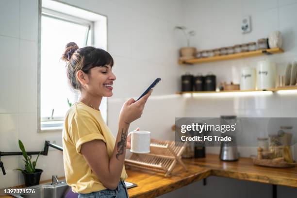 young woman using the mobile phone while drinking coffee or tea at home - coffee chat stockfoto's en -beelden