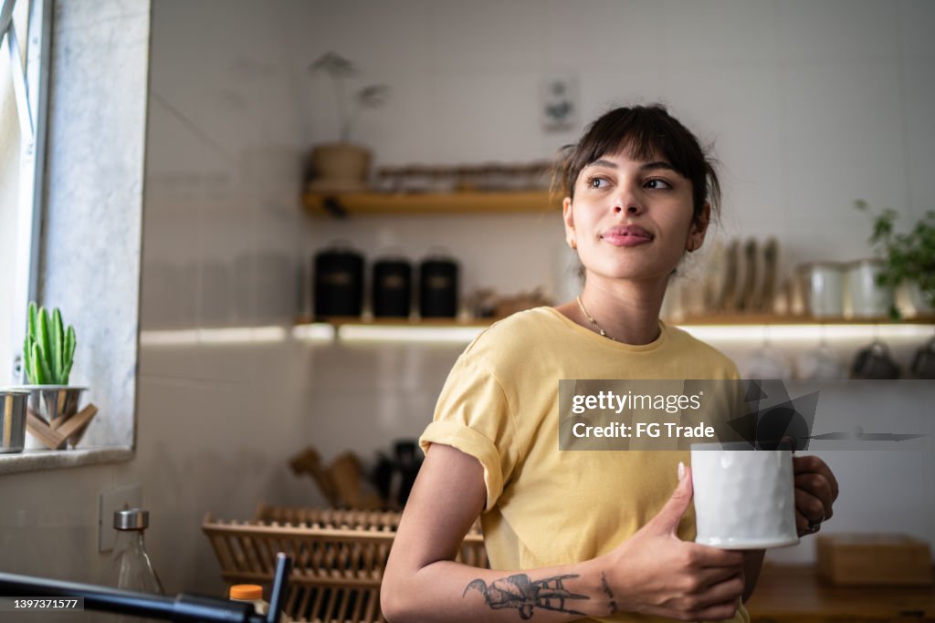 Jeune femme contemplative buvant du café ou du thé et regardant la fenêtre à la maison