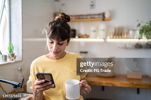 Young woman using the mobile phone while drinking coffee or tea at home Young woman using the mobile phone while drinking coffee or tea at home