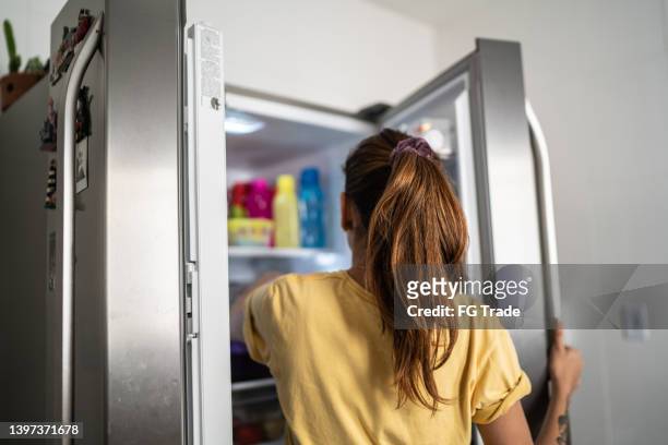 vista trasera de una mujer joven con la puerta del refrigerador abierta - congelador fotografías e imágenes de stock