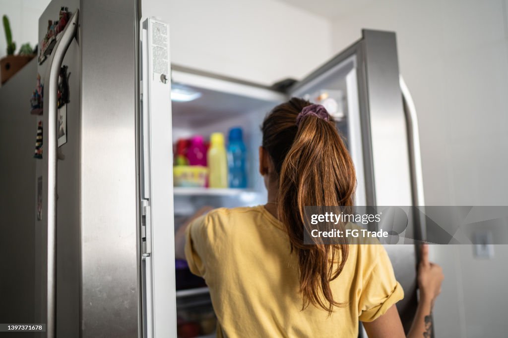 Rear view of a young woman with refrigerator door open