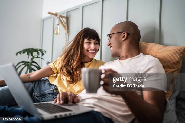 jeune couple utilisant l’ordinateur portable dans le lit à la maison - happy millennial at home photos et images de collection