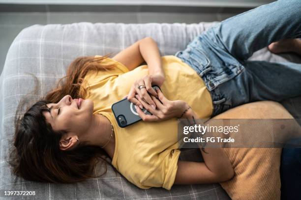 young woman lying down in the bed holding the mobile phone at home - verliefd worden stockfoto's en -beelden