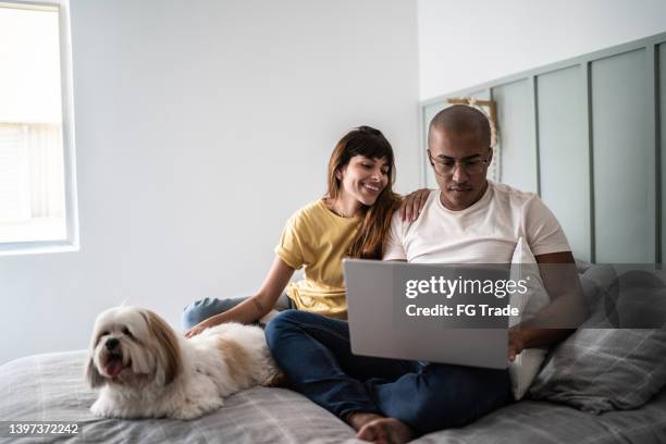 junges paar, das den laptop mit dem hund im bett zu hause benutzt - mann frau hund zuhause stock-fotos und bilder