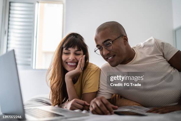 young couple watching something on the laptop in bed at home - young couple at movie together imagens e fotografias de stock