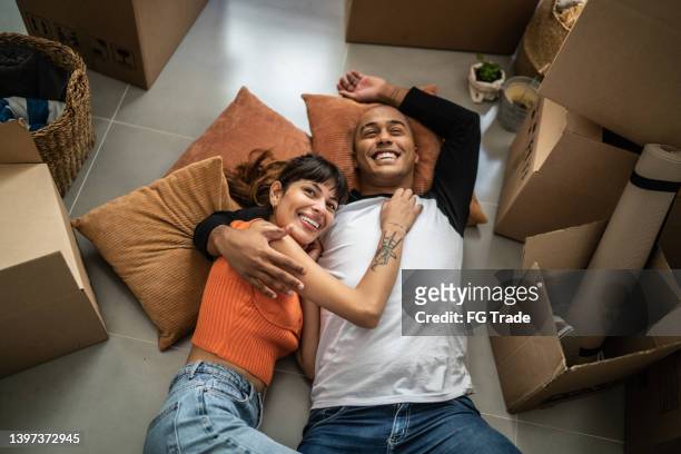 feliz pareja joven tirada en el suelo en una nueva casa - estrenar casa fotografías e imágenes de stock