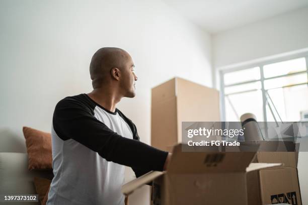 young man moving house, looking away contemplating while packing moving boxes - memories box stock pictures, royalty-free photos & images