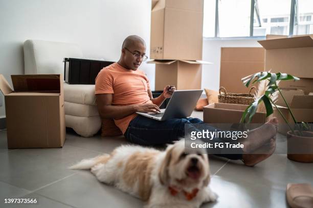young man doing online shopping using laptop at new home - man laptop dog stock pictures, royalty-free photos & images