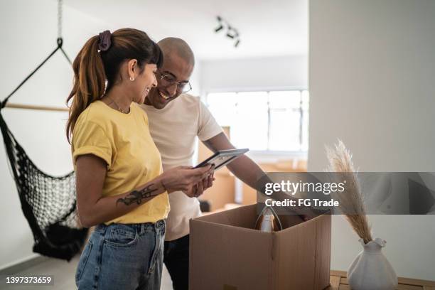 young couple packing and moving boxes and looking for frame photo at new home - memories box stock pictures, royalty-free photos & images