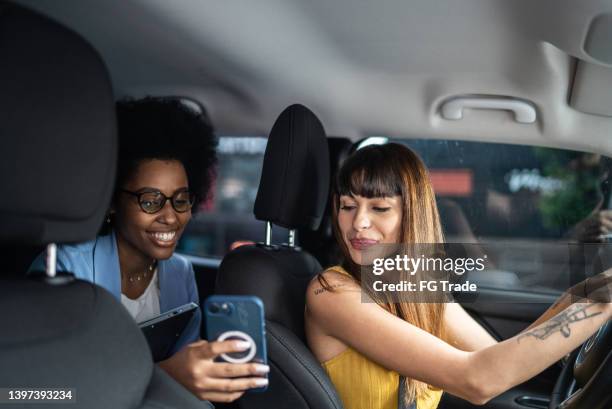 passenger talking to cab driver and showing her the smartphone - sharing economy stockfoto's en -beelden