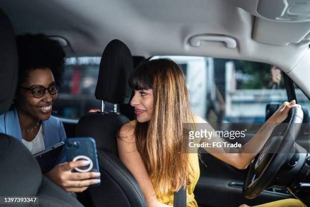 passenger talking to cab driver and showing her the smartphone - taxi driver stock pictures, royalty-free photos & images