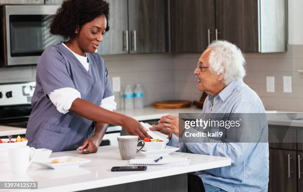 home caregiver helps senior man in kitchen - nutritionist stock pictures, royalty-free photos & images