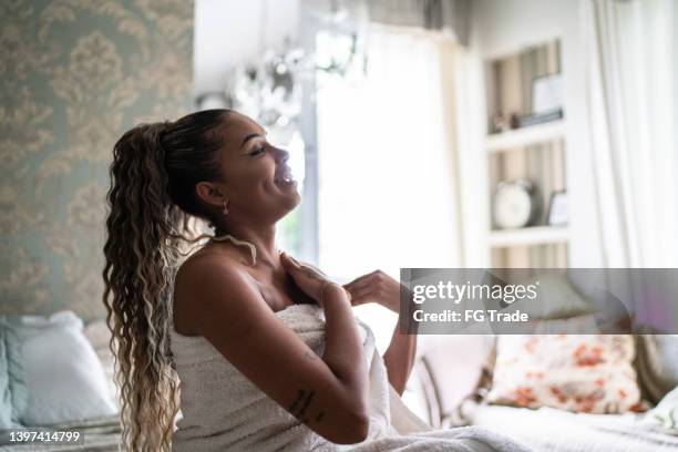 young woman applying moisturizer on the body at home - beautiful women bed stockfoto's en -beelden