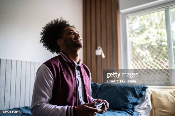 contemplative young man holding a video game controller while packing belongings - pre game stockfoto's en -beelden