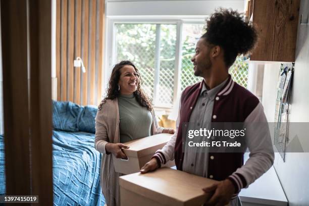mother helping son carrying moving boxes to move out from parent's home - studentenflats stockfoto's en -beelden