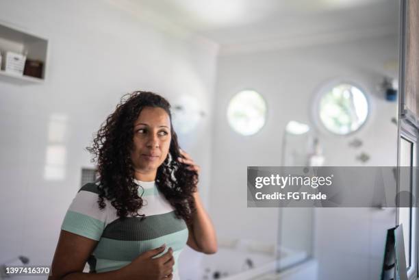 mid adult woman taking care of her hair while looking on mirror at home - woman brushing hair stockfoto's en -beelden