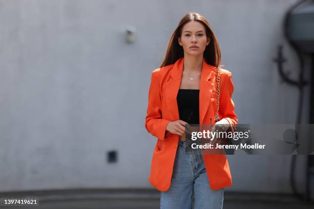 Marie von der Ahe is seen wearing a blue denim jeans, a black cropped top, a orange blazer, silver necklace and black sunglasses and a orange handbag...