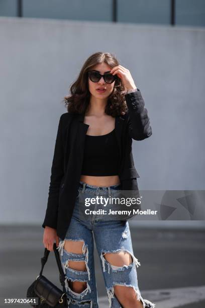 Tuana Koc is seen wearing a black blazer, a black top, a blue denim with cut outs, black loafer and a black Guess mini leather handbag and sunglass...