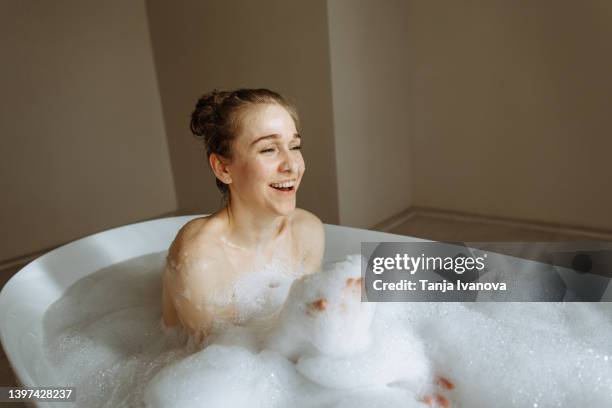 young beautiful woman taking in bubble bath and plays with foam and bubbles - woman bath bubbles stock-fotos und bilder