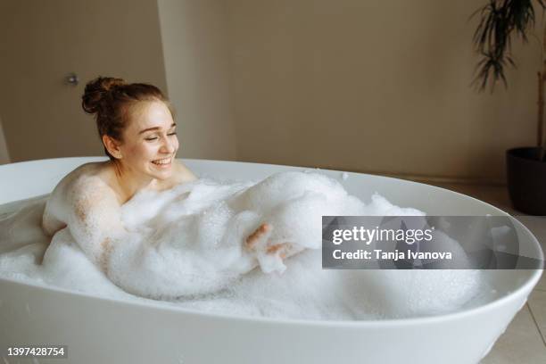 young beautiful woman taking in bubble bath and plays with foam and bubbles - woman bath bubbles stock-fotos und bilder