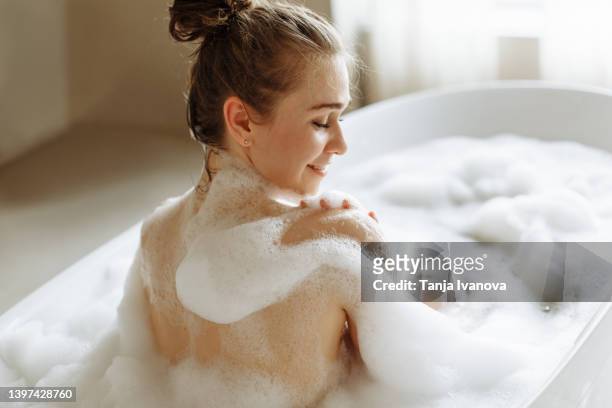 back view of a young beautiful woman enjoying a bubble bath - bath bubble stockfoto's en -beelden