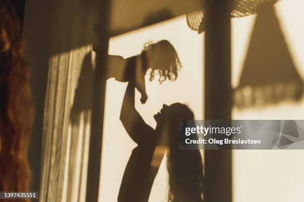 family fun. beautiful shadows on wall of mom playing with her daughter. childhood concept, harmony in family - baby light stock-fotos und bilder