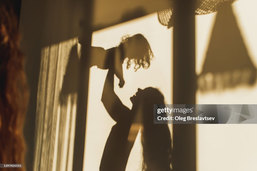 Family fun. Beautiful shadows on wall of mom playing with her daughter. Childhood concept, harmony in family