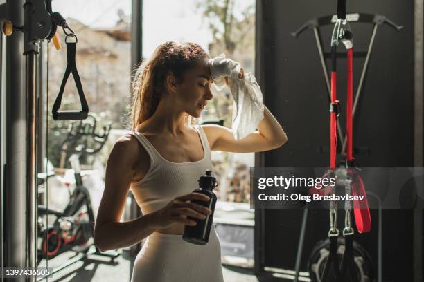 woman tired after workout in gym, drinking water and wiping off sweat from forehead. - fragilidad fotografías e imágenes de stock