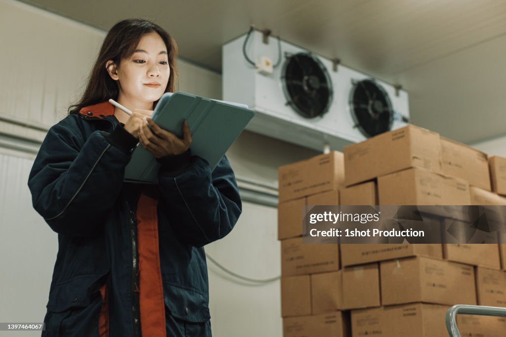 Travailleuse de l’entreposage frigorifique utilisant une tablette numérique pour vérifier les stocks.