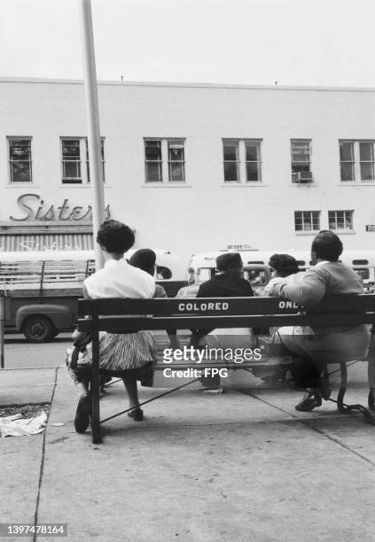 Rear view of a group of five women sitting on a bench on which 'Colored Only' is written, in Lakeland, Florida, circa 1955. A sign for the Lake...
