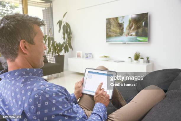man using smart home automation in living room with digital tablet - adjusting stock pictures, royalty-free photos & images